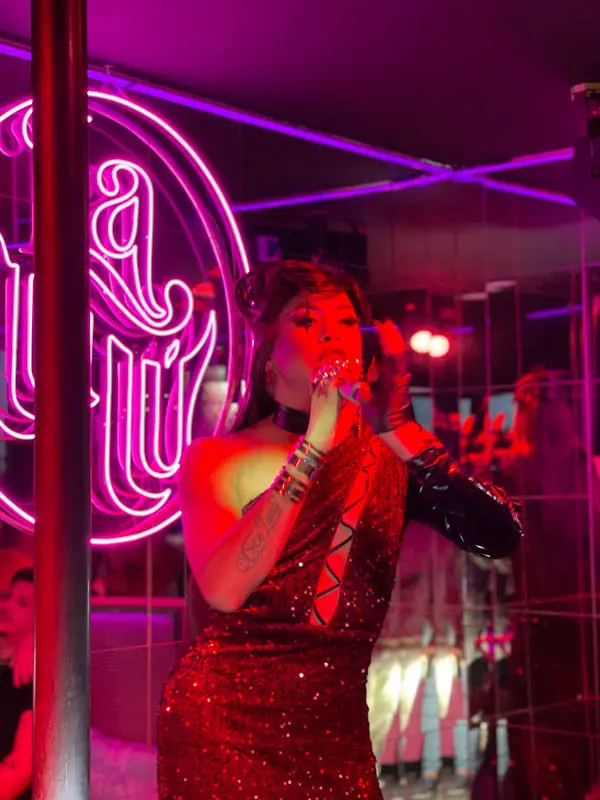 Drag queen realizando un show en LulÃƒÂº Show Bar, con el logotipo de neÃƒÂ³n rosa al fondo.